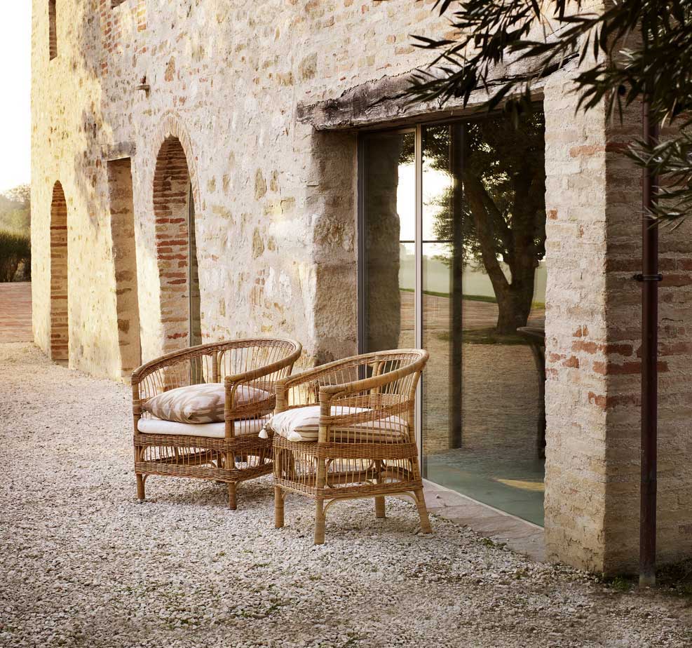 Two rattan chairs in front of a historic brick facade and quarried stonework of a renovated finca.